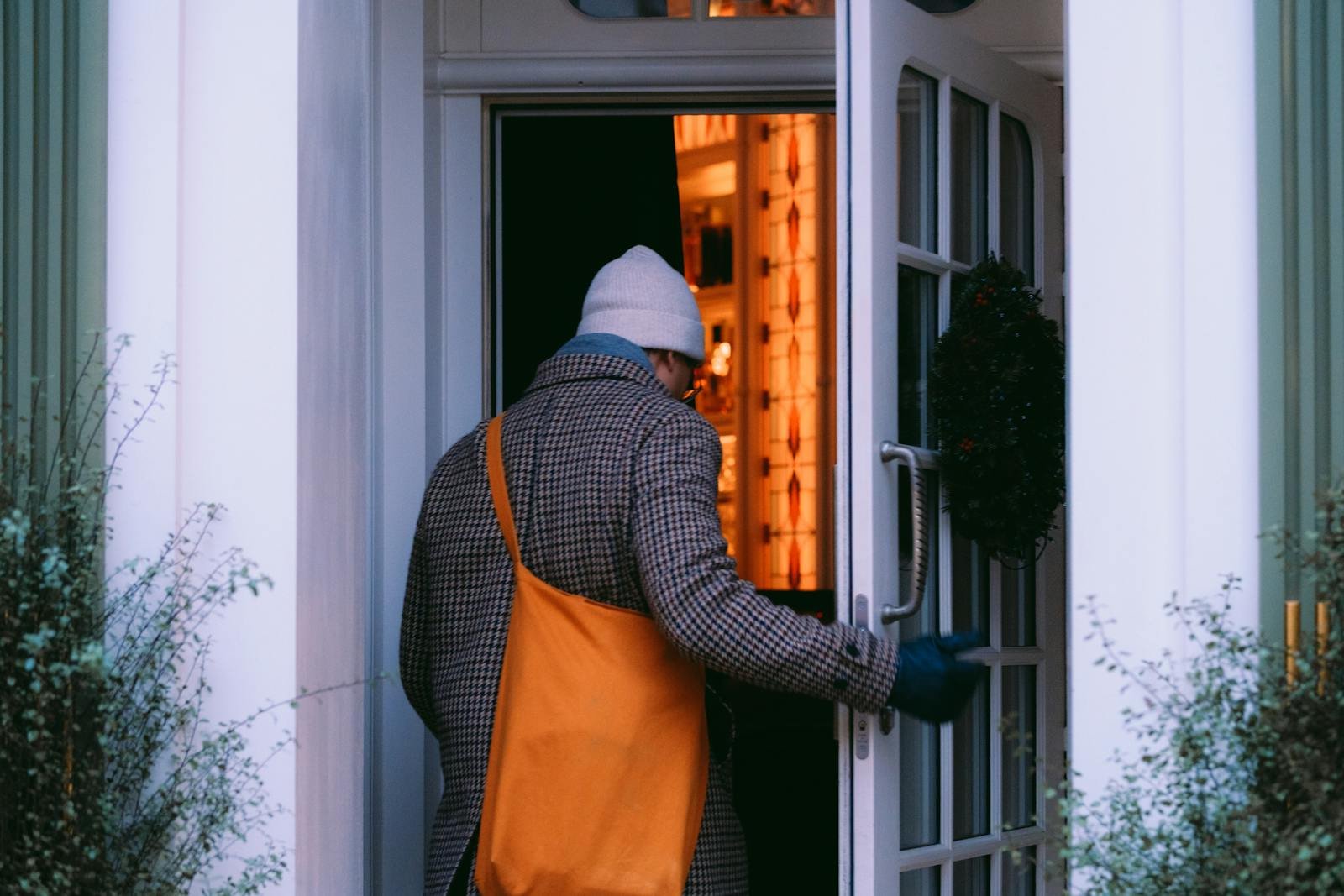 A person in winter attire enters a warmly lit home through a decorated door.